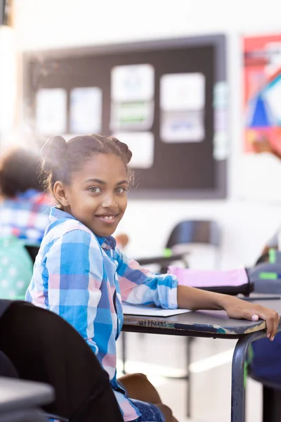 坐在课桌前的一个笑着的女生的竖向肖像 在教室的复制空间里转过来 包容性 小学教育 学习概念 — 图库照片