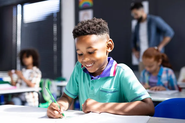 小学校の教室でデスクで書いているアフリカ系アメリカ人の小学生の笑顔 コミュニティ 小学校 学習コンセプト — ストック写真