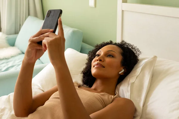 一个带耳机的女人用智能手机躺在床上躺在卧室里 生活方式 交流和家庭生活 — 图库照片