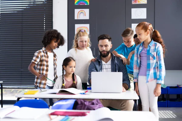 男性教師の周りの多様な小学生は 教室の机でノートパソコンを使用して スペースをコピーします コミュニティ 小学校 学習コンセプト — ストック写真
