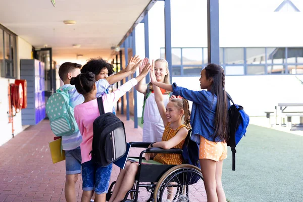 Okul Koridorunda Tekerlekli Sandalyedeki Kızla Beşlik Çakışan Çeşitli Okul Çocukları — Stok fotoğraf