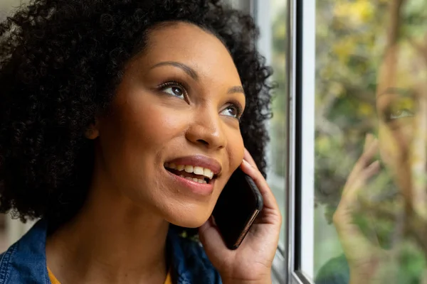 Glad Biracial Kvinna Talar Smartphone Och Tittar Genom Fönstret Hemma — Stockfoto