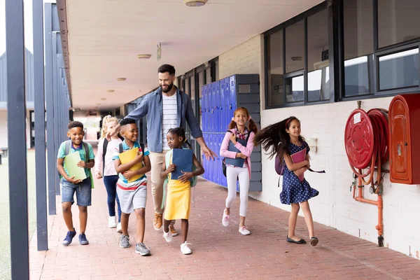 Çeşitli Mutlu Erkek Öğretmenler Okul Koridorunda Yürüyen Ilkokul Çocukları Kopya — Stok fotoğraf