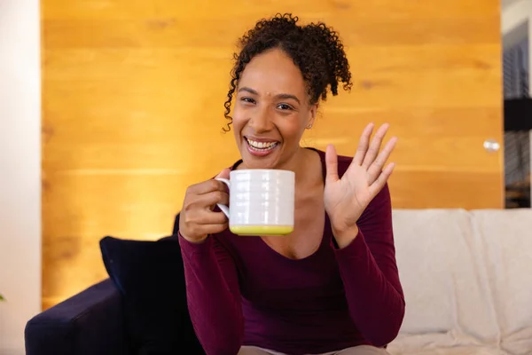 Gelukkige Biracial Vrouw Met Kopje Koffie Maken Videogesprek Zwaaien Woonkamer — Stockfoto