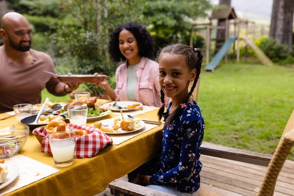Portret Szczęśliwej Dwurasowej Córki Przy Stole Jedzącej Posiłek Rodzicami Ogrodzie — Zdjęcie stockowe