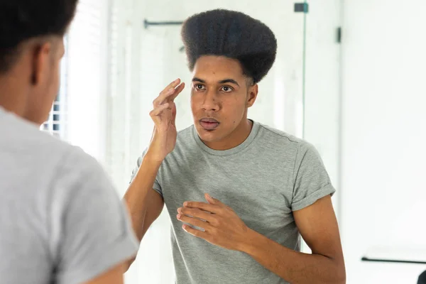 Homem Biracial Olhando Espelho Inspecionando Rosto Olhos Banheiro Ensolarado Autocuidado — Fotografia de Stock