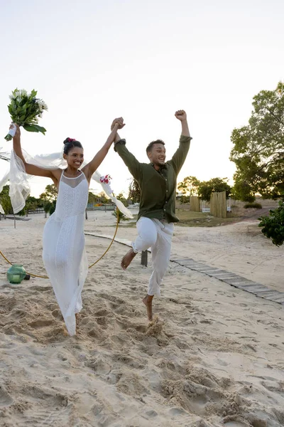 Newlywed Biracial Couple Jumping Cheerfully Sandy Beach Clear Sky Wedding — Stock Photo, Image