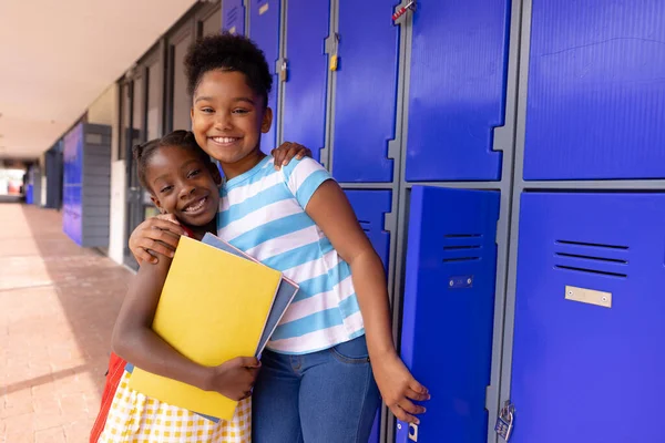 Portrait of happy african american schoolchildren standing next to locker at school. Education, childhood, elementary school and learning concept.