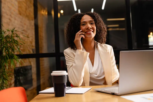 快乐的非洲裔美国女商人使用笔记本电脑 在办公室里用智能手机聊天 临时办公室 通信和工作 未经改动 — 图库照片