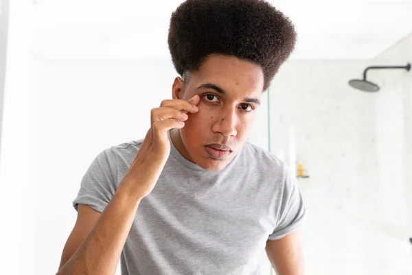 Homem Biracial Olhando Espelho Inspecionando Olhos Banheiro Ensolarado Autocuidado Bem — Fotografia de Stock