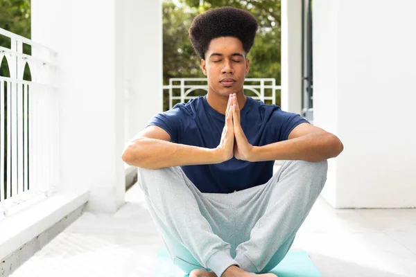 stock image Relaxed biracial man practicing yoga meditation sitting on balcony. Wellbeing, fitness and healthy lifestyle, unaltered.