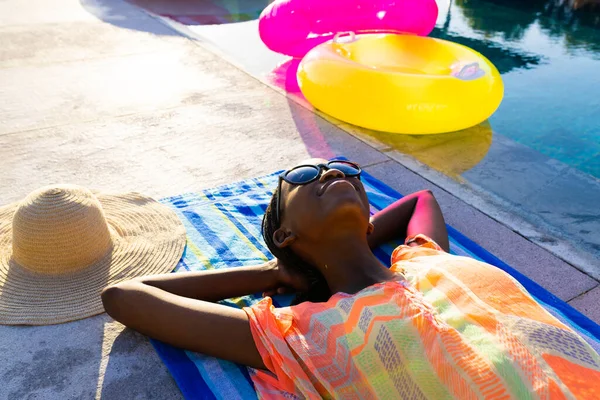 庭のプールの横にあるタオルと日光浴に横たわっている幸せなアフリカ系アメリカ人女性 ライフスタイル 自由な時間と休暇 変わらない — ストック写真
