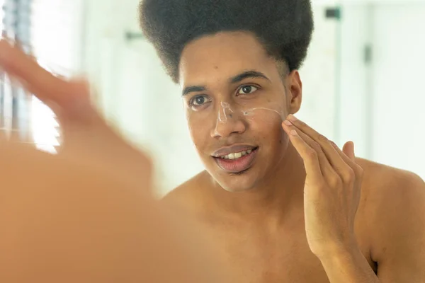 Glad Biracial Man Tittar Spegeln Och Tillämpa Ansiktskräm Soligt Badrum — Stockfoto
