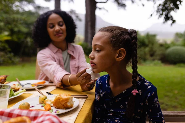 庭で食事中に娘の顔をきれいにテーブルに座って幸せな出産の母親 子供時代 食べ物 ライフスタイル 変わらない — ストック写真