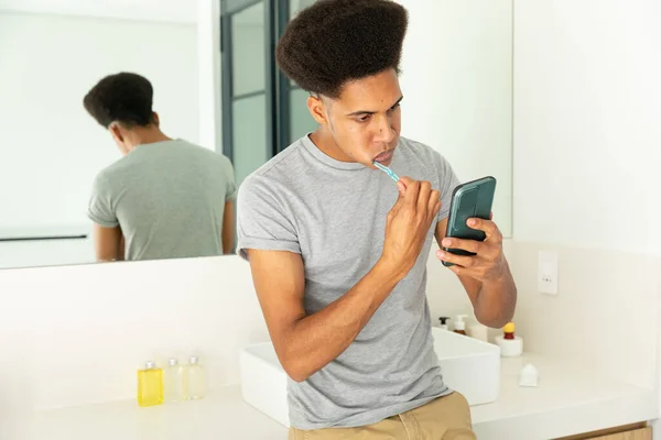 Zweirassiger Mann Beim Zähneputzen Und Smartphone Sonnigen Badezimmer Selbstpflege Zahnpflege — Stockfoto