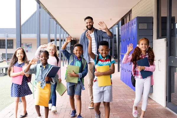 Diverse Gelukkige Mannelijke Leraar Basisschoolkinderen Zwaaiend Schoolgang Kopieerruimte Onderwijs Inclusiviteit — Stockfoto