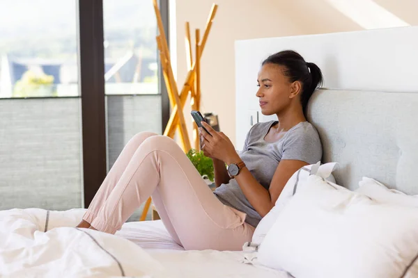 Biracial Kobieta Pomocą Smartfona Łóżku Sypialni Relaks Styl Życia Komunikacja — Zdjęcie stockowe