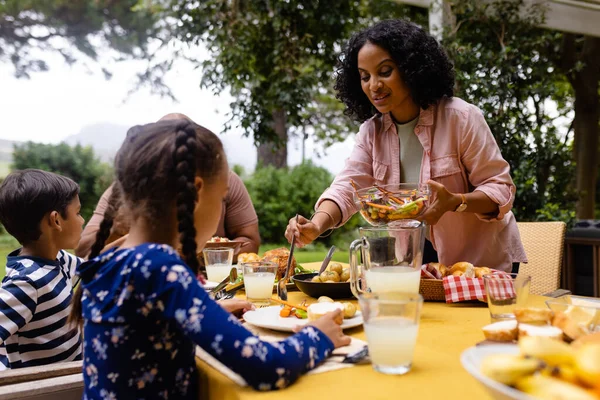 幸せな出産の両親 娘は食べ物を提供し 庭で食事をするためにテーブルに座っています 一緒に 食べ物とライフスタイル 変わらない — ストック写真