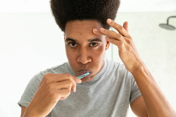 Homem Biracial Olhando Espelho Escovando Dentes Inspecionando Pele Banheiro Ensolarado — Fotografia de Stock