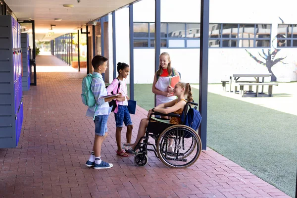 学校の廊下で車椅子で女の子と話す コピースペースで幸せな多様な学校の子供たち コミュニティ 小学校 学習コンセプト — ストック写真