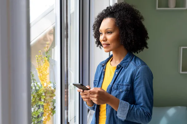Happy Biracial Woman Using Smartphone Looking Out Window Home Lifestyle — Stock Photo, Image