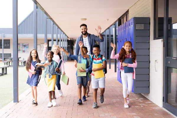 Diverse Happy Male Teacher Elementary Schoolchildren Waving School Corridor Copy — Stock Photo, Image