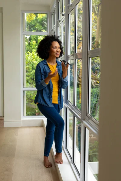 Mujer Birracial Feliz Hablando Teléfono Inteligente Mirando Por Ventana Casa —  Fotos de Stock