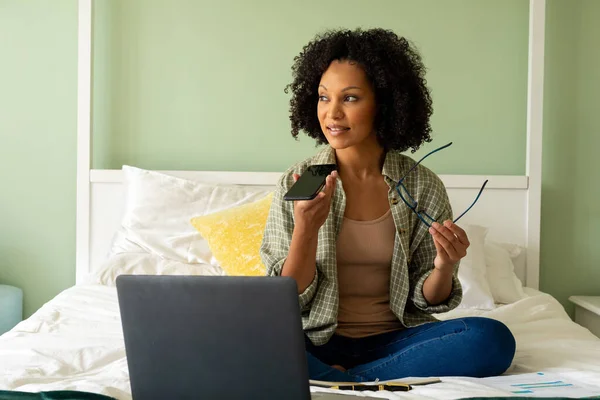 Çift Irklı Kadın Dizüstü Bilgisayar Kullanıyor Yatakta Akıllı Telefonla Konuşuyor — Stok fotoğraf