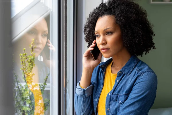 Dwurasowa Kobieta Rozmawiająca Przez Smartfona Wyglądająca Przez Okno Domu Styl — Zdjęcie stockowe