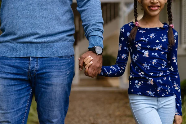 stock image Midsection of biracial father and smiling daughter holding hands in garden outside house. Family, love, togetherness, home, lifestyle and domestic life, unaltered.