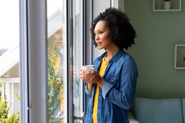 一个漂亮的女人举着一杯咖啡 望着窗外的家 生活方式和家庭生活 — 图库照片