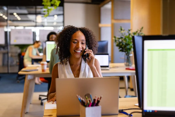 Счастливая Расовая Случайная Деловая Женщина Использующая Ноутбук Разговаривающая Смартфоне Офисе — стоковое фото