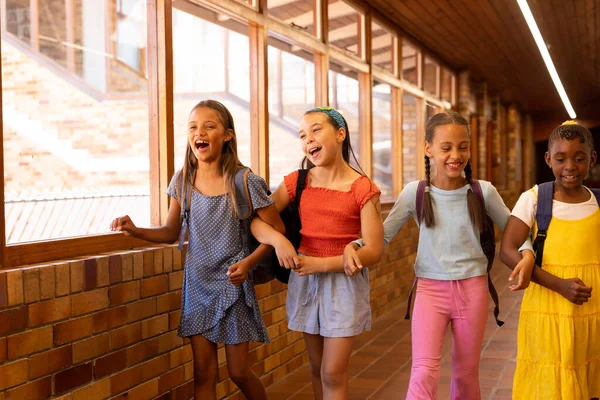 Sokszínű Boldog Iskolás Lányok Táskákkal Akik Általános Iskolai Folyosón Sétálnak — Stock Fotó