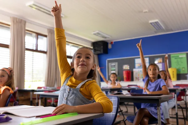 Feliz Diversas Alunas Sentadas Mesas Levantando Mãos Sala Aula Escola — Fotografia de Stock