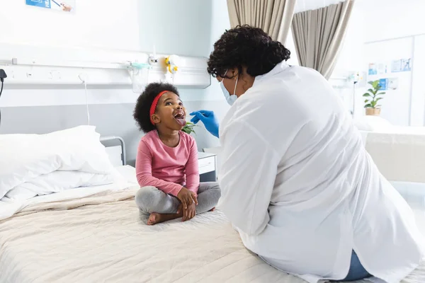 アフリカ系アメリカ人女性医師が病院で少女患者を診察するフェイスマスクを着用 医学および医療 変更されていない — ストック写真