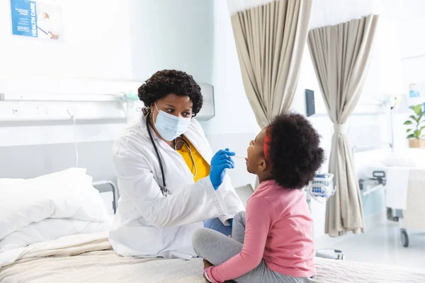 非洲裔美国女医生戴着口罩在医院检查女病人 医药和保健 未经改动 — 图库照片