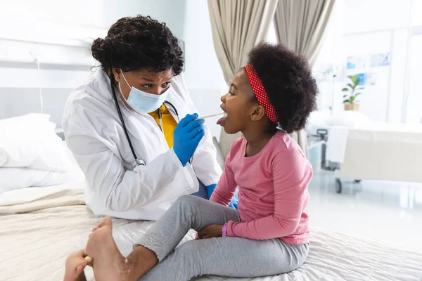 アフリカ系アメリカ人女性医師が病院で少女患者を診察するフェイスマスクを着用 医学および医療 変更されていない — ストック写真