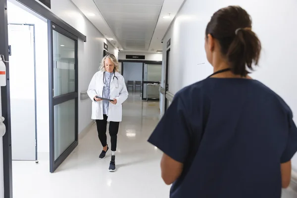 病院の廊下を歩くタブレットを使用する白人女性医師 障害者 コミュニケーション 変わらない — ストック写真