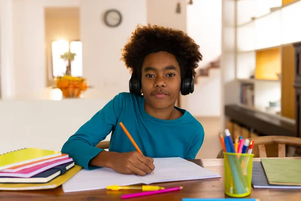 ハッピーアフリカ系アメリカ人の少年がオンライン授業を受けるテーブルに座ってメモを取る 子供時代 コミュニケーション 家庭生活 変わらない — ストック写真