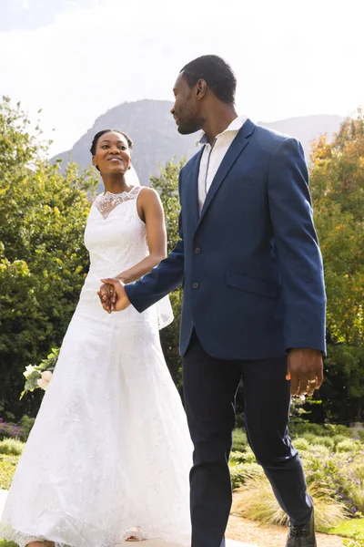 Feliz Novia Afroamericana Novio Tomados Mano Caminando Jardín Soleado Matrimonio —  Fotos de Stock