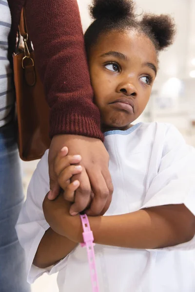 Sad african american girl patient and her mother holding hands in corridor at hospital. Hospital, motherhood, family, medicine and healthcare, unaltered.