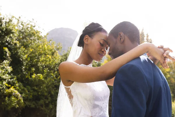Happy african american bride and groom embracing at wedding in sunny garden. Marriage, romance, summer, tradition, ceremony, nature and lifestyle, unaltered.