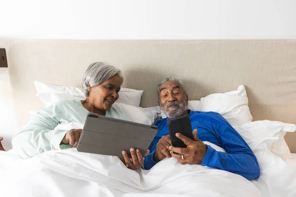 Feliz Casal Biracial Sênior Deitado Cama Usando Tablet Smartphone Casa — Fotografia de Stock