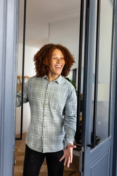Happy caucasian man with curly hair welcoming at door at home. Domestic life and lifestyle, unaltered.