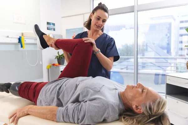 Caucasian female physiotherapist and senior woman with artificial leg stretching at hospital. Hospital, disability, physiotherapy, work, medicine and healthcare, unaltered.