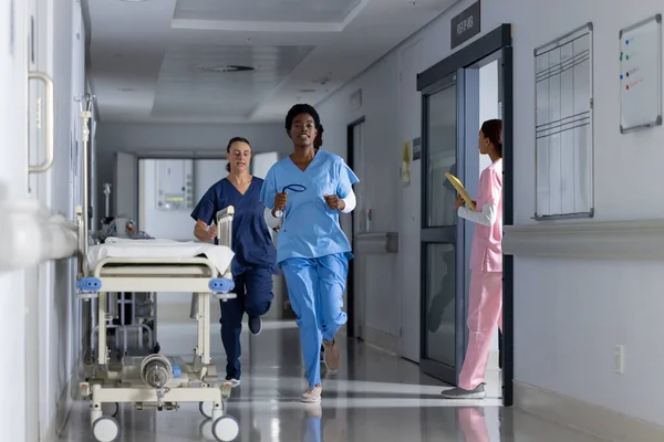 Diverse doctors wearing scrubs running through corridor at hospital. Hospital, teamwork, medicine, healthcare and work, unaltered.