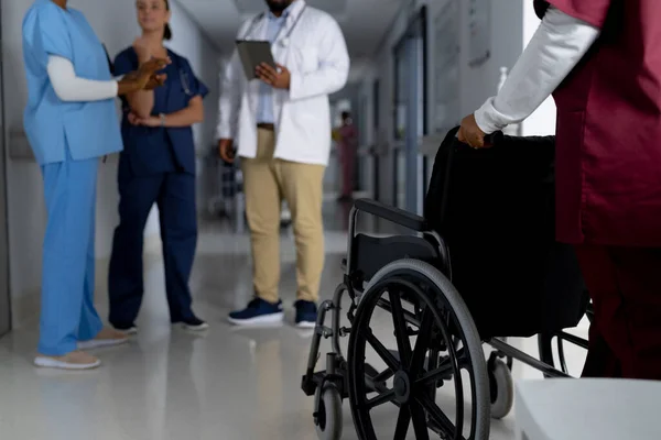 African american female doctor walking with wheelchair in corridor at hospital. Hospital, medicine, healthcare and work, unaltered.