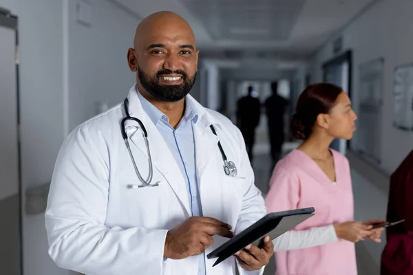 Retrato Homem Birracial Feliz Usando Jaleco Segurando Tablet Corredor Hospital — Fotografia de Stock