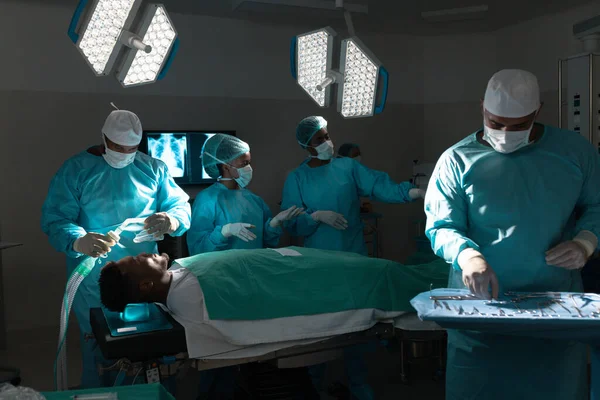 Diverse surgeons wearing surgical gowns operating on patient in operating theater at hospital. Hospital, surgery, hygiene, teamwork, medicine, healthcare and work, unaltered.