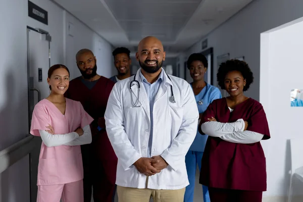 Portrait of happy diverse doctors standing in corridor at hospital. Hospital, medicine, teamwork, healthcare and work, unaltered.